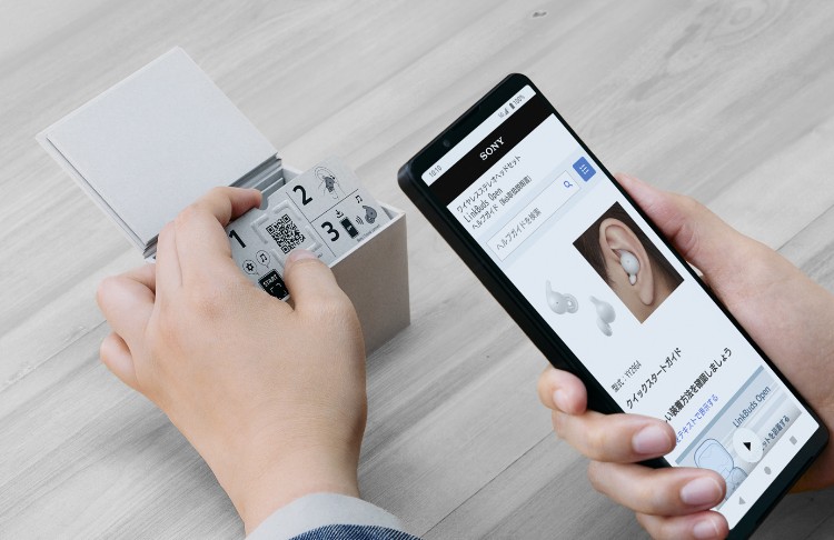 An image of a person holding the Sony LinkBuds Open packaging and scanning the QR code with a smartphone.